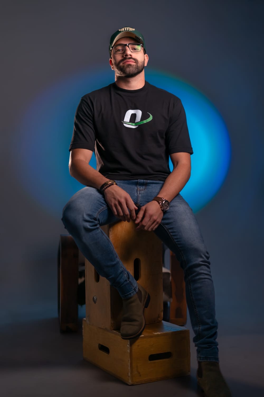 Pedro Oliveira sentado em estúdio, usando boné e camiseta preta